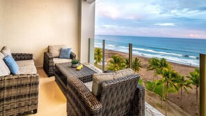 Un balcone con mobili in vimini, un tavolino con una pianta e vista sulla spiaggia e sull'oceano.