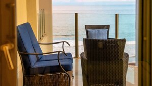 Un balcone con due sedie in vimini e una poltrona imbottita blu, con vista su un corpo d'acqua.