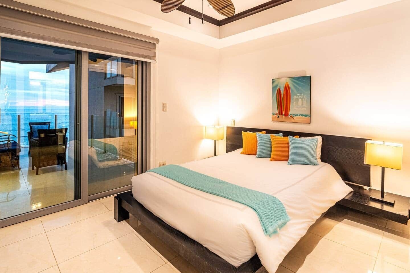 Een hotelkamer met een bed, twee bedlampen, een schilderij aan de muur en uitzicht door een glazen deur.