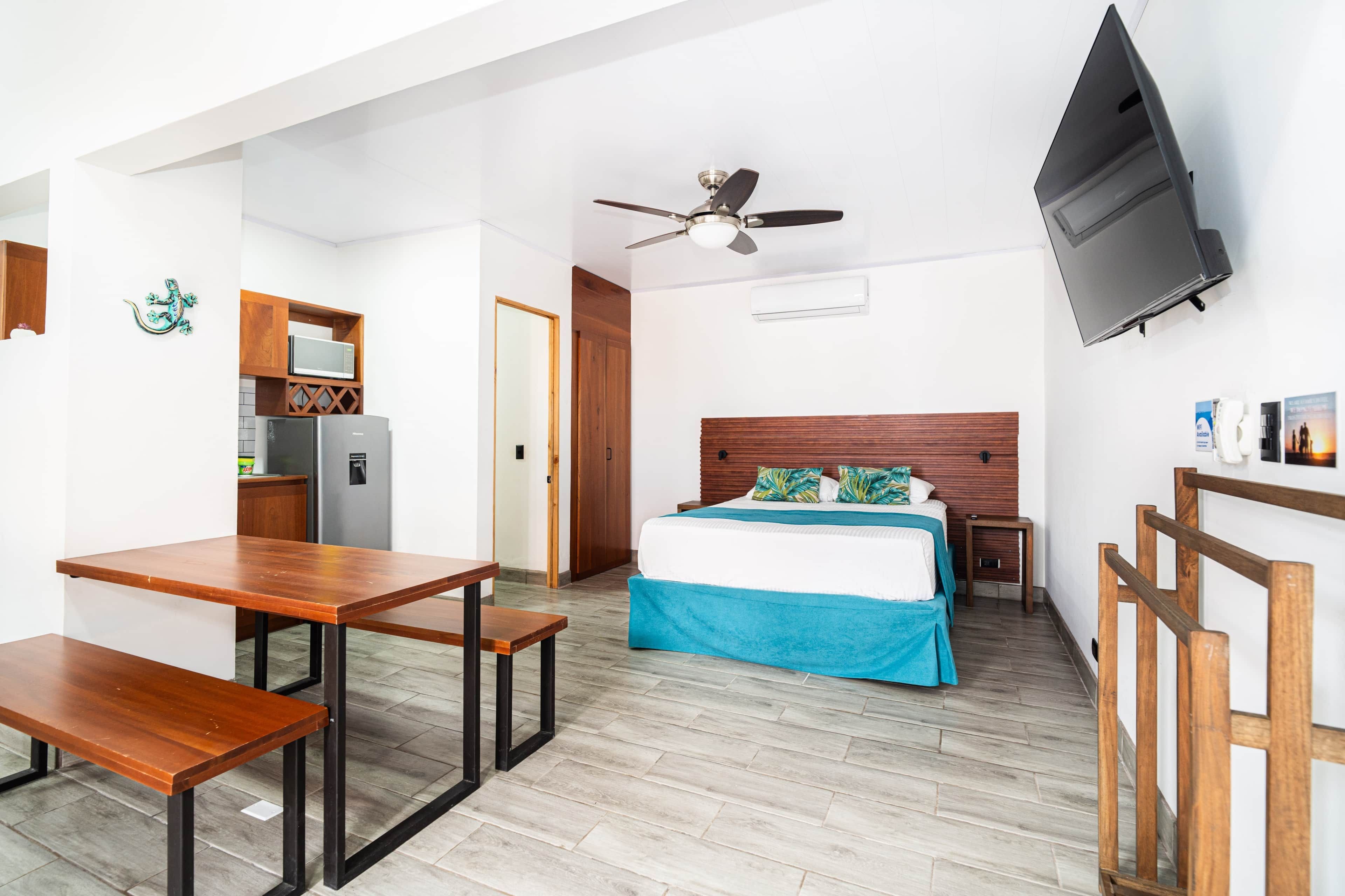 A hotel room with a bed, a desk, a chair, a TV, and a kitchenette.