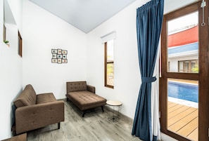 A room with a sofa, a chair, a small round table, and a view of a swimming pool through a large window. - Villa Favare - 10 Private Suites in Downtown Jaco (Jaco)