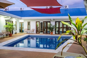A pool area with a clear blue pool, wooden deck, and potted plants. - Villa Favare - 10 Private Suites in Downtown Jaco (Jaco)