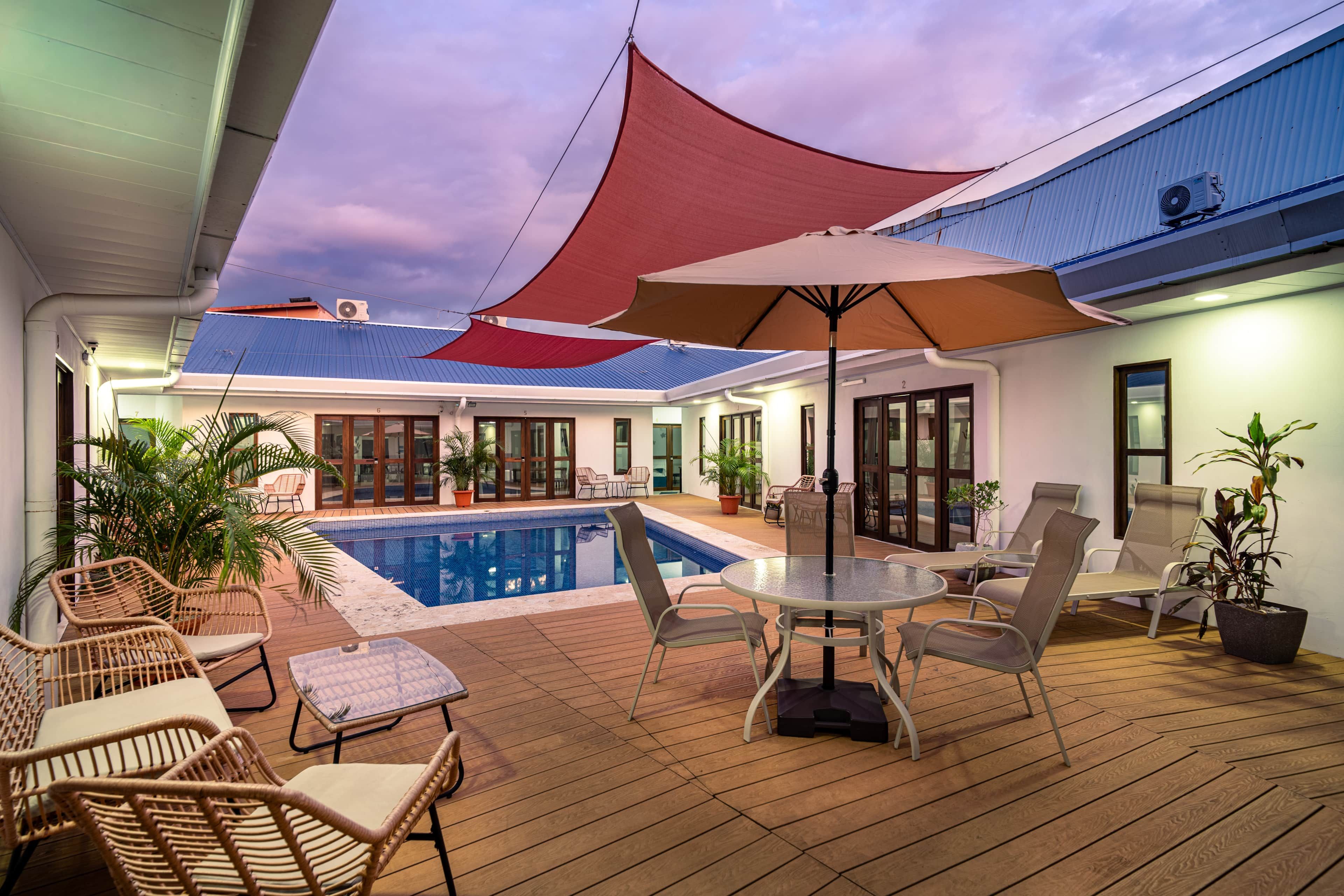 A covered outdoor area with a pool, lounge chairs, and umbrellas.