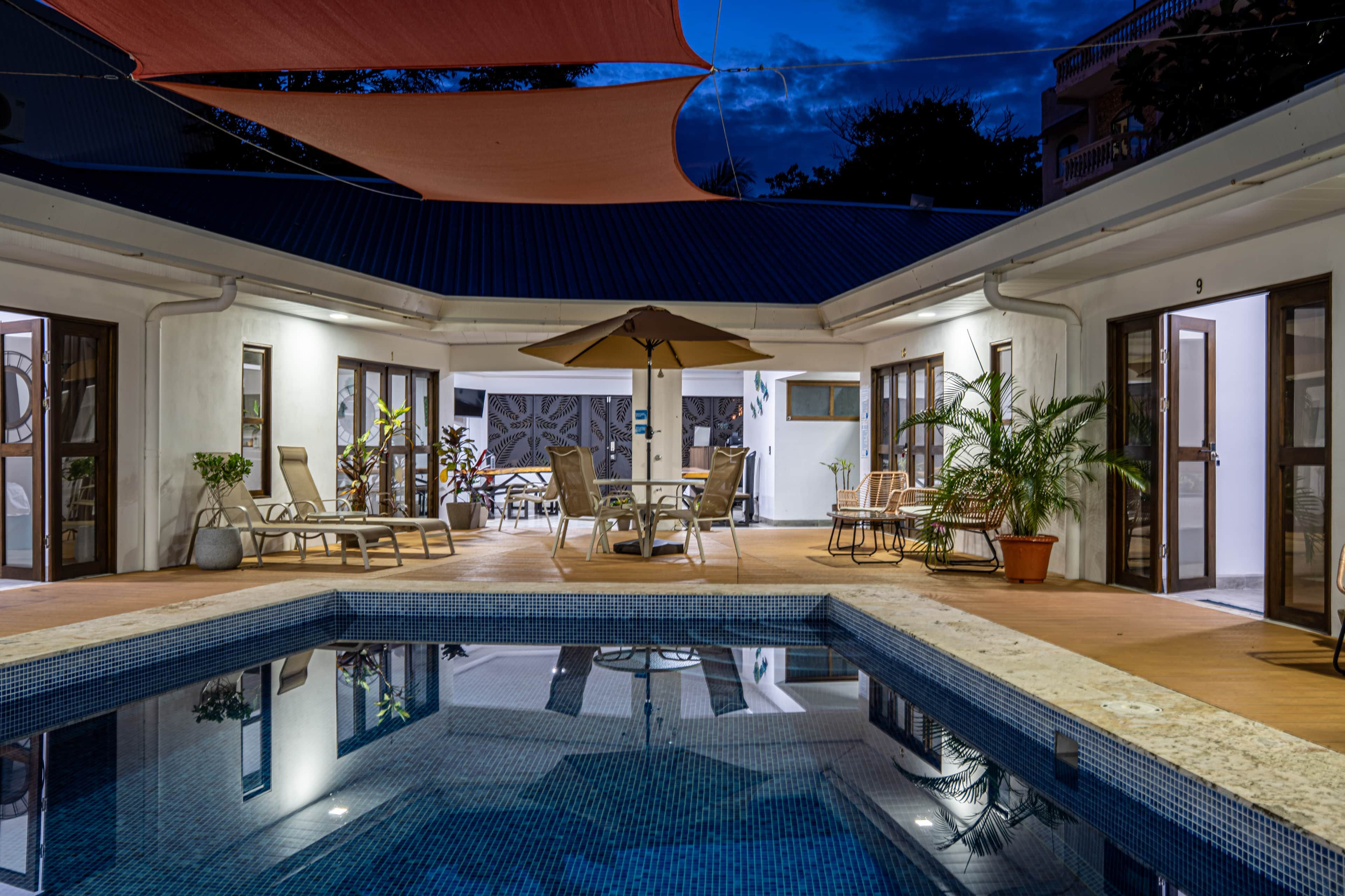 Ein Pool mit Liegestühlen und Sonnenschirmen, umgeben von einer  überdachten Terrasse.
