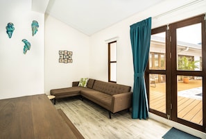 A modern living room with a sectional sofa, a dining table, and a large window with curtains. - Villa Favare - 10 Private Suites in Downtown Jaco (Jaco)