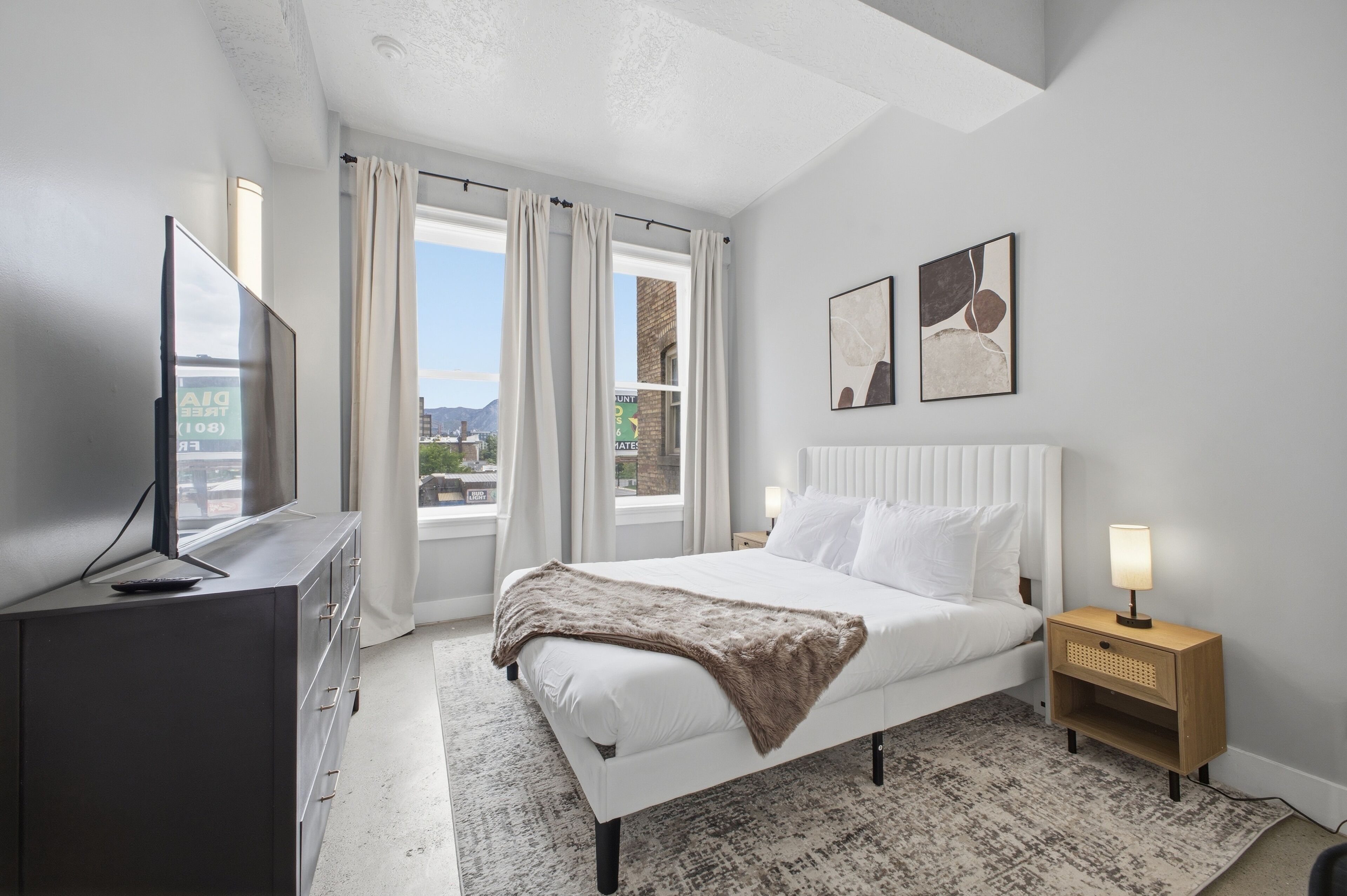 Een slaapkamer met een bed, een televisie, een nachtkastje en een raam met gordijnen.