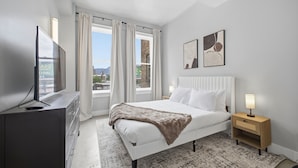 Ein Schlafzimmer mit Bett, Fernseher, Nachttisch und einem Fenster mit Vorhängen.