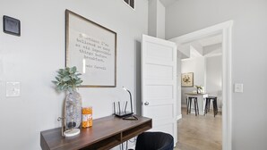 Ein modernes Zimmer mit Schreibtisch, Stuhl, gerahmtem Zitat und einer Tür zu einem weiteren Raum.