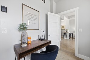 Ein modernes Zimmer mit Schreibtisch, Stuhl, gerahmtem Zitat und einer Tür zu einem weiteren Raum.
