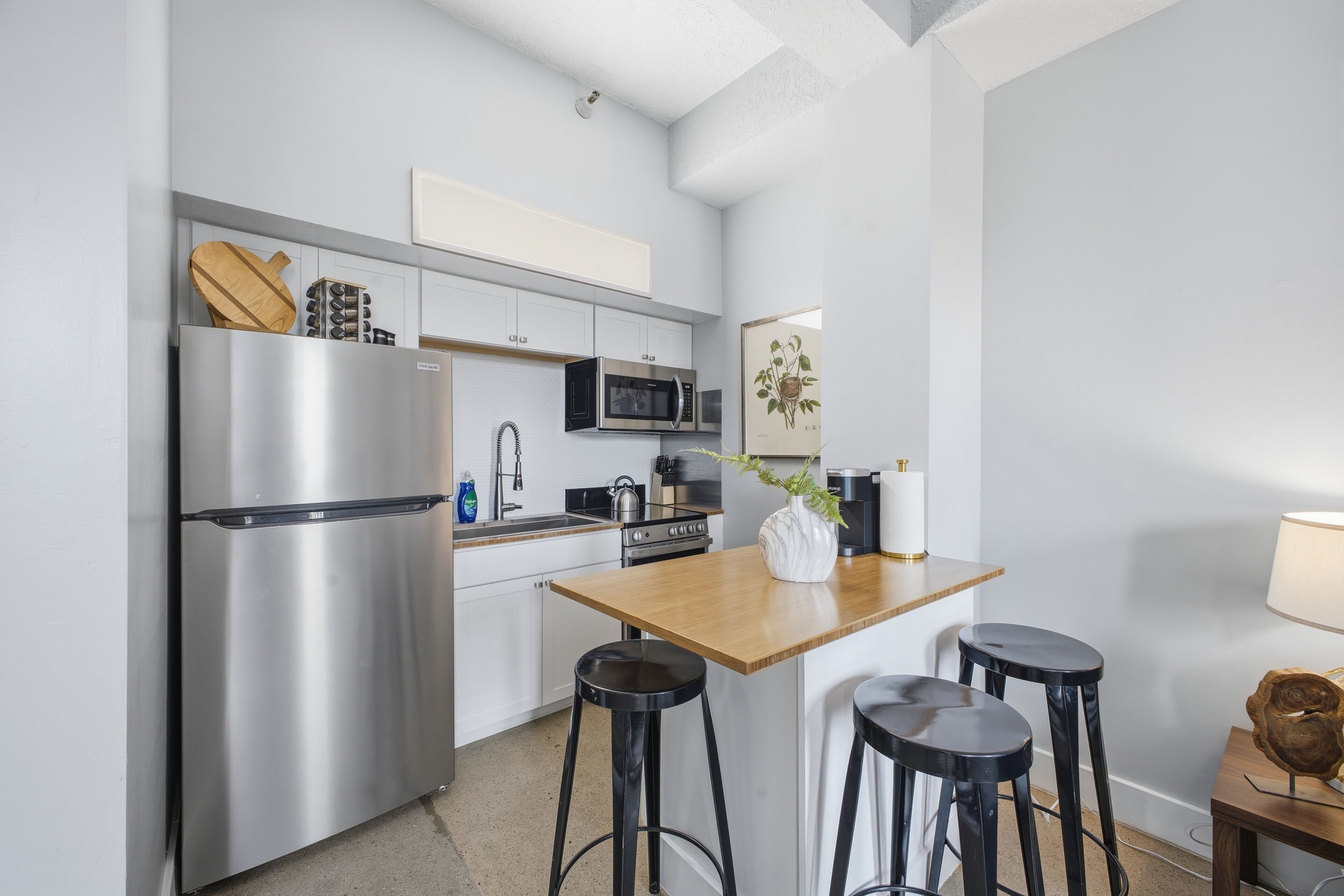 Een moderne keuken met roestvrijstalen apparatuur, een houten tafel en zwarte barkrukken.
