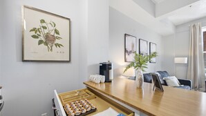 Ein modernes Hotelzimmer mit Schreibtisch aus Holz, einer Kaffeemaschine, einer Pflanze und einem gerahmten botanischen Druck an der Wand.