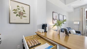 Een moderne hotelkamer met een houten bureau, een koffiezetapparaat, een plant en een ingelijste botanische illustratie aan de muur.
