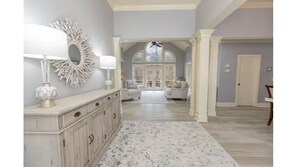 Un vaste espace de vie agrémenté d’un grand miroir, d’une console blanche et d’un tapis à motifs.