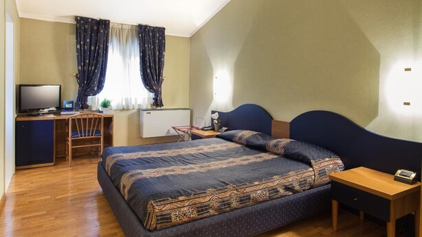 A bedroom with a bed, a desk, a chair, a television, and a window with curtains. - Hotel Gambara (Gambara)