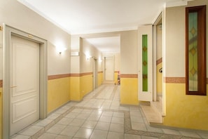 Un passadís d'hotel amb portes, lluminàries i un terra de rajoles.