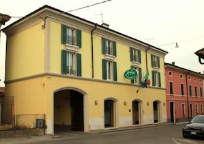 A yellow building with green shutters, a sign indicating it's a hotel, and a flag. - Hotel Gambara (Gambara)
