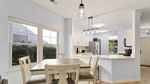 Een moderne keuken met een centraal eiland, witte keukenkastjes en een eethoek met een houten tafel en stoelen.