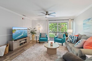 A living room with a television, two blue armchairs, a beige sofa, a round coffee table, and a ceiling fan. - Cozy 2-bedroom 2nd floor, end unit condo in charming Sarasota (Sarasota)