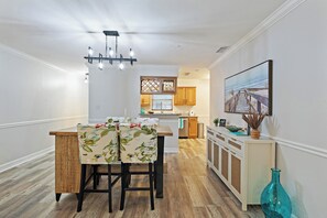 Eine moderne Küche mit Holzboden, einer Essecke mit zwei Stühlen, einer Pendelleuchte und einem Gemälde an der Wand.