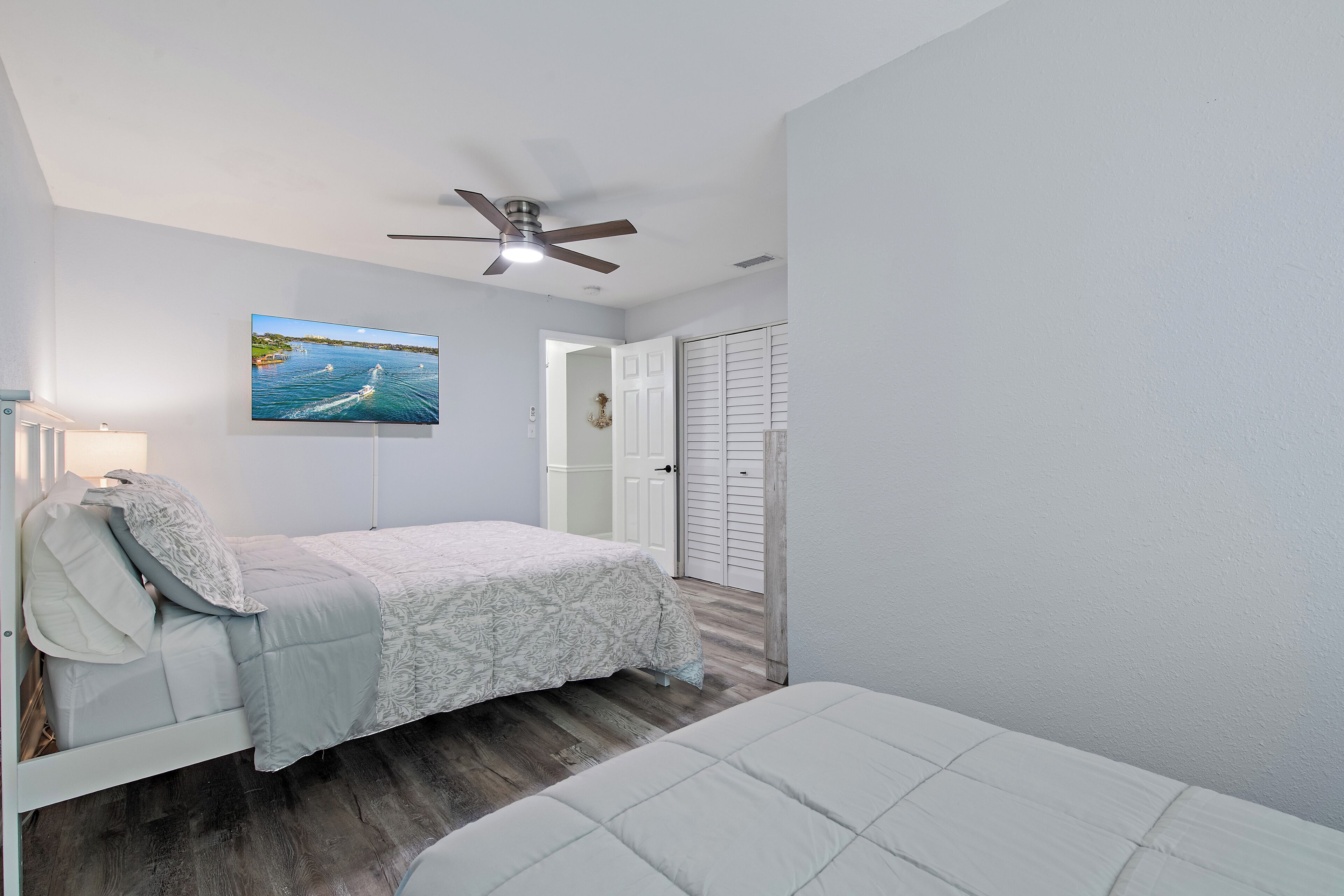 A bedroom with a bed, a ceiling fan, a TV on the wall, and a door leading to a closet.