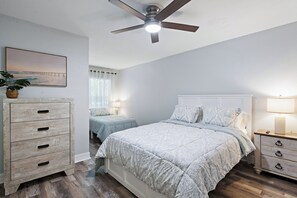 Ein Schlafzimmer mit Bett, Nachttischen, Deckenventilator, Kommode und einem Gemälde an der Wand.