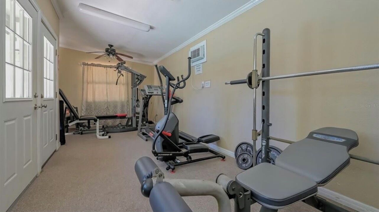 Une salle de sport équipée de matériel d’exercice, avec un ventilateur au plafond et une fenêtre avec des rideaux.