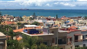 A coastal residential area with buildings, a view of the sea, and a distant ship.