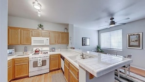 A kitchen with wooden cabinets, a white countertop, a stove, a microwave, and a ceiling fan.