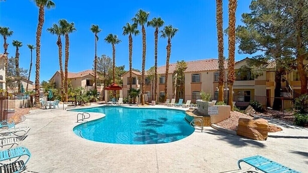 A swimming pool surrounded by palm trees and buildings with a clear blue sky.