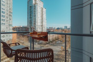 Un balcon avec des fauteuils en osier et une table, d’où l’on peut admirer une vue sur la ville, avec ses nombreux immeubles.
