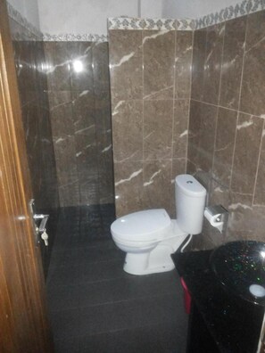A bathroom with a toilet, a bidet, and a black trash bin. - RF Hotel (Cisarua)