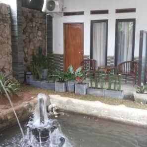 A stone wall, a water feature, potted plants, and a wooden door. - RF Hotel (Cisarua)