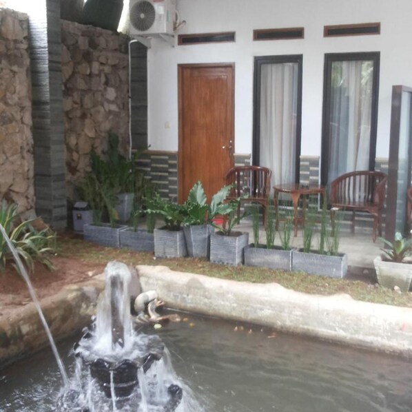 A stone wall, a water feature, potted plants, and a wooden door. - RF Hotel (Cisarua)