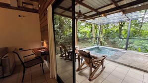 Um quarto com parede de vidro, uma cadeira de balanço de madeira, uma mesinha e um chão ladrilhado.