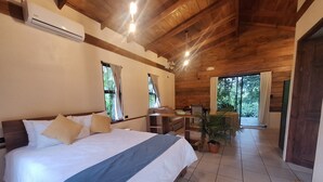 Quarto com cama, escrivaninha, cadeira, planta em vaso e vista para o exterior.