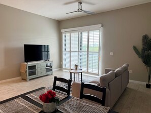 Ein Wohnzimmer mit Flachbildfernseher, einer Couch, einem Esstisch mit Blumenvase und einer Schiebeglastür.