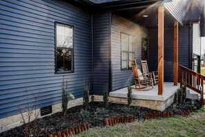 Ein Haus mit verdeckter Veranda, einem kleinen Garten und einer Holztreppe.