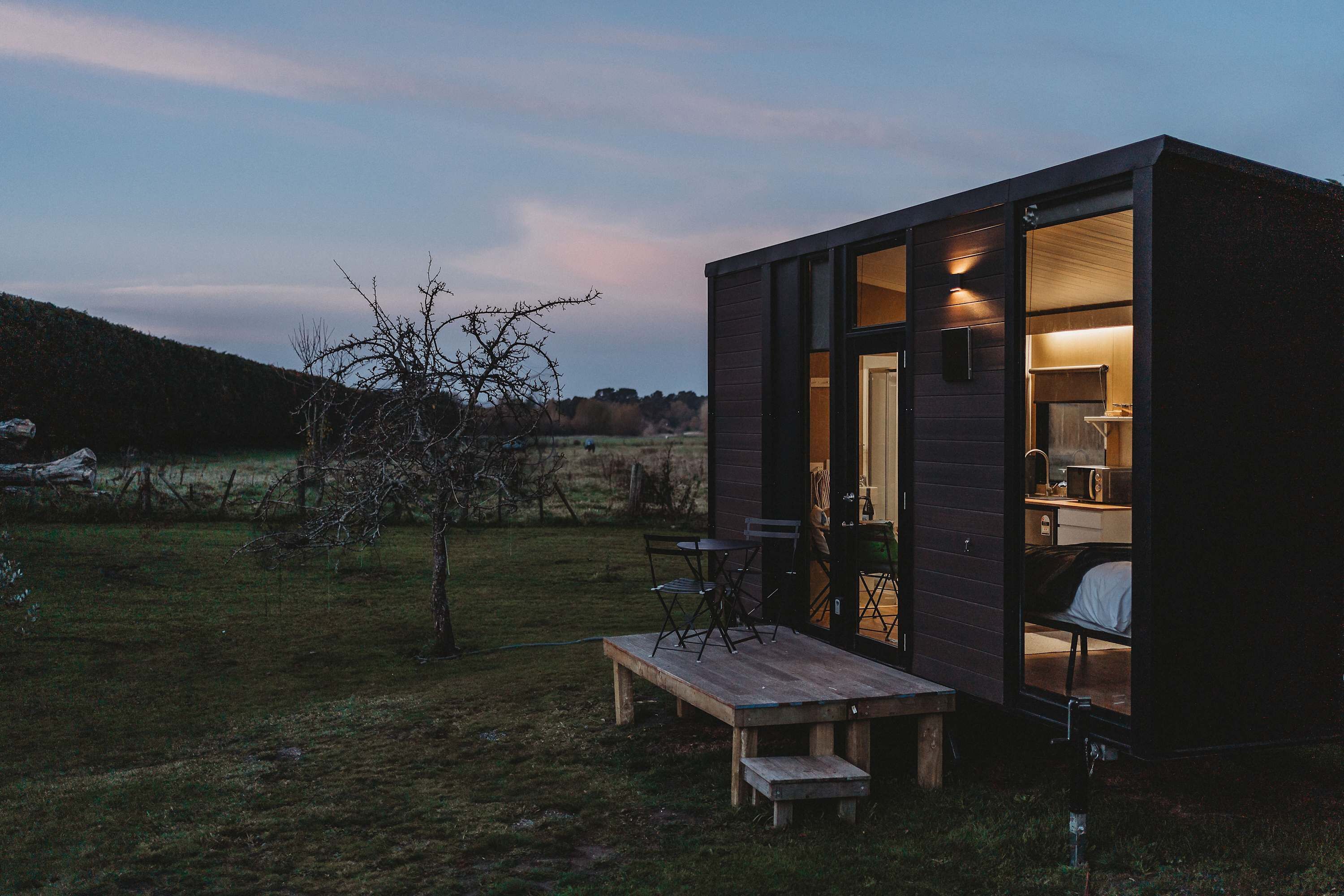 A small, modern cabin with a wooden deck, a table, and chairs outside.