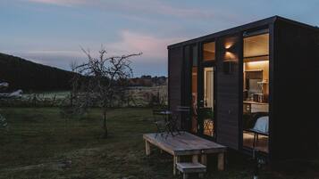 A small, modern cabin with a wooden deck, a table, and chairs outside.