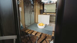 A compact kitchen with a glass door, a white sink, and a wooden table with a fruit basket.