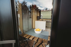 A compact kitchen with a glass door, a white sink, and a wooden table with a fruit basket.