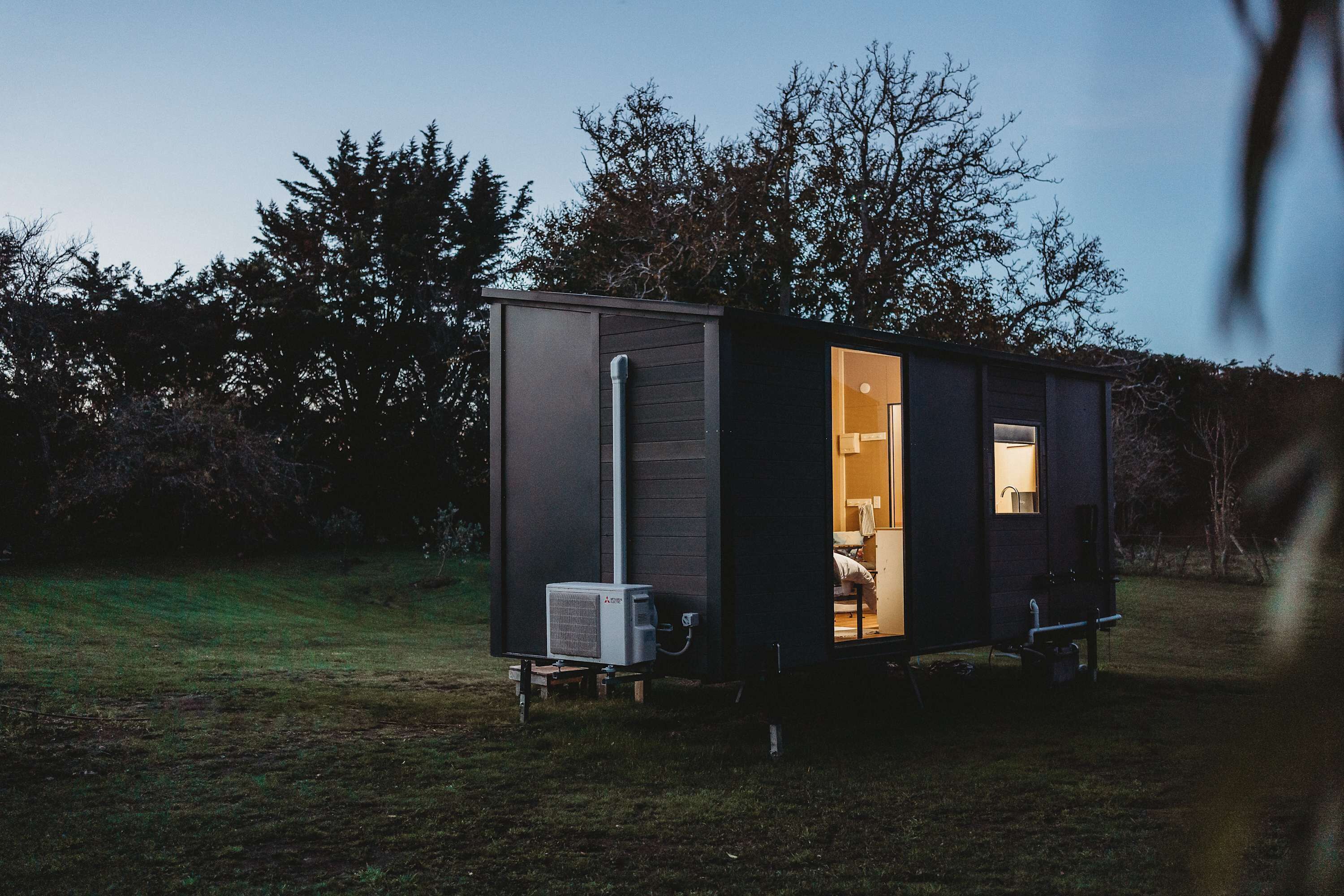 A small, dark-colored portable structure with an open door revealing a room with a bed and a window.