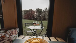 A view from inside a room to an outdoor seating area with a table, chairs, and a bottle of wine.