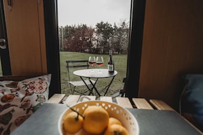 A view from inside a room to an outdoor seating area with a table, chairs, and a bottle of wine.