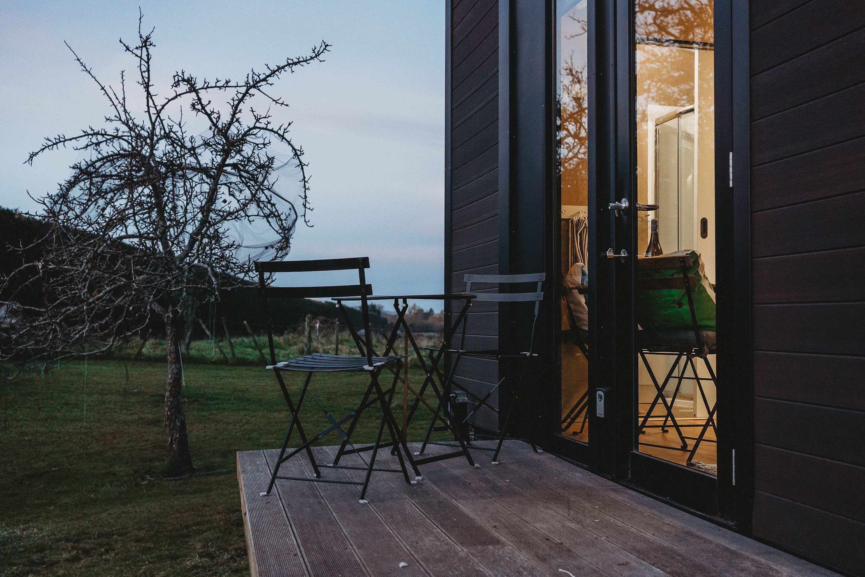 A wooden deck with outdoor furniture, a tree, and a building entrance.