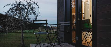 A wooden deck with outdoor furniture, a tree, and a building entrance.