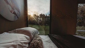 A bedroom with a bed, a fluffy rug, a painting on the wall, and a view of trees and grass outside.