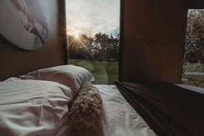 A bedroom with a bed, a fluffy rug, a painting on the wall, and a view of trees and grass outside.