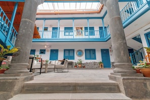 Un patio con una escalera que lleva a un balcón, plantas en macetas y una zona de estar con mesa y sillas.