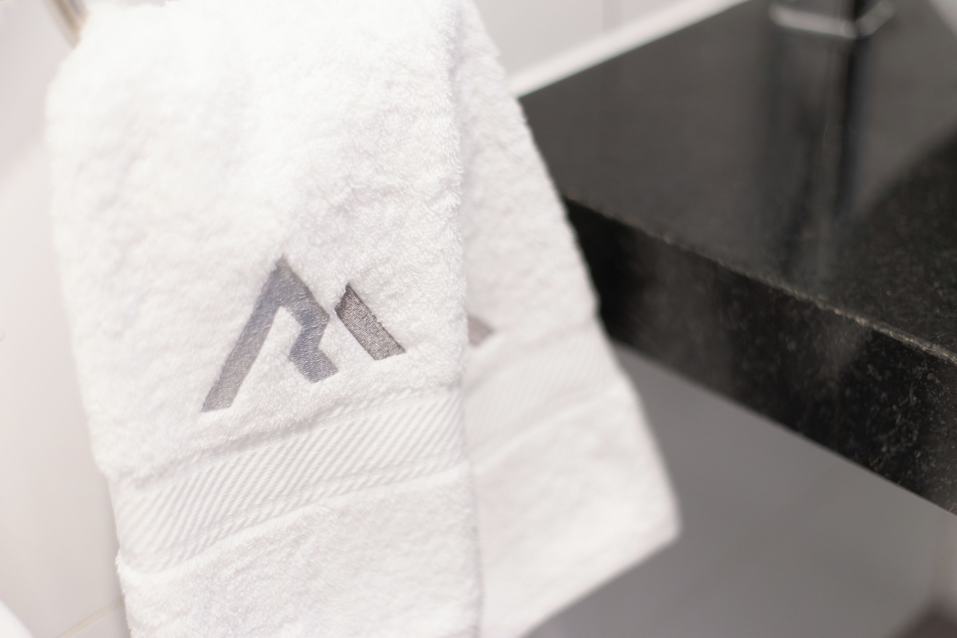 Una toalla blanca con un logotipo gris sobre una encimera de baño.